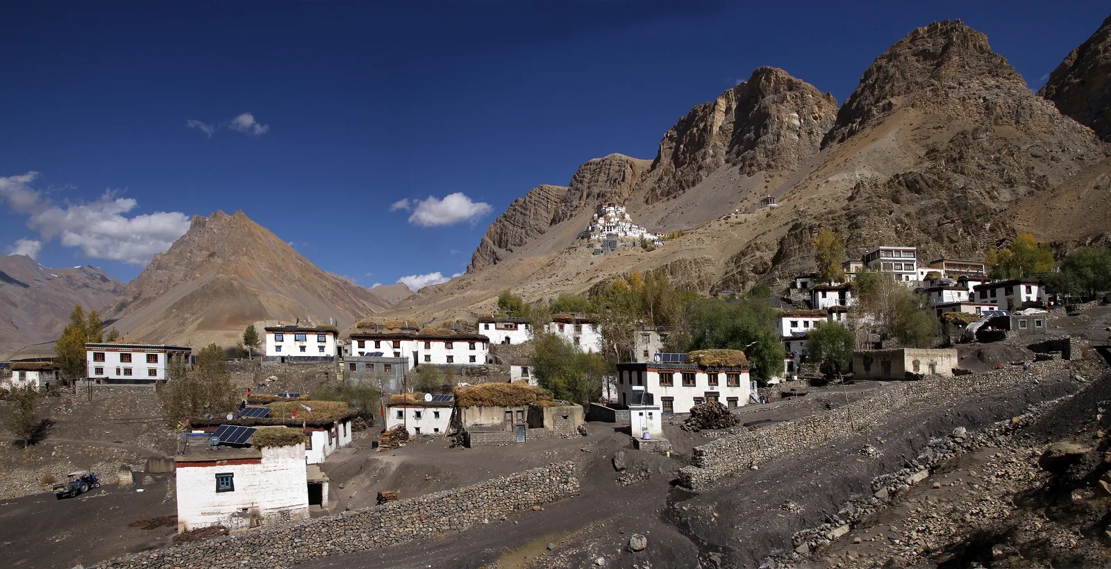 White-walled houses of Key village below the rocky hill of Key Monastery in Spiti under a blue sky with a few clouds