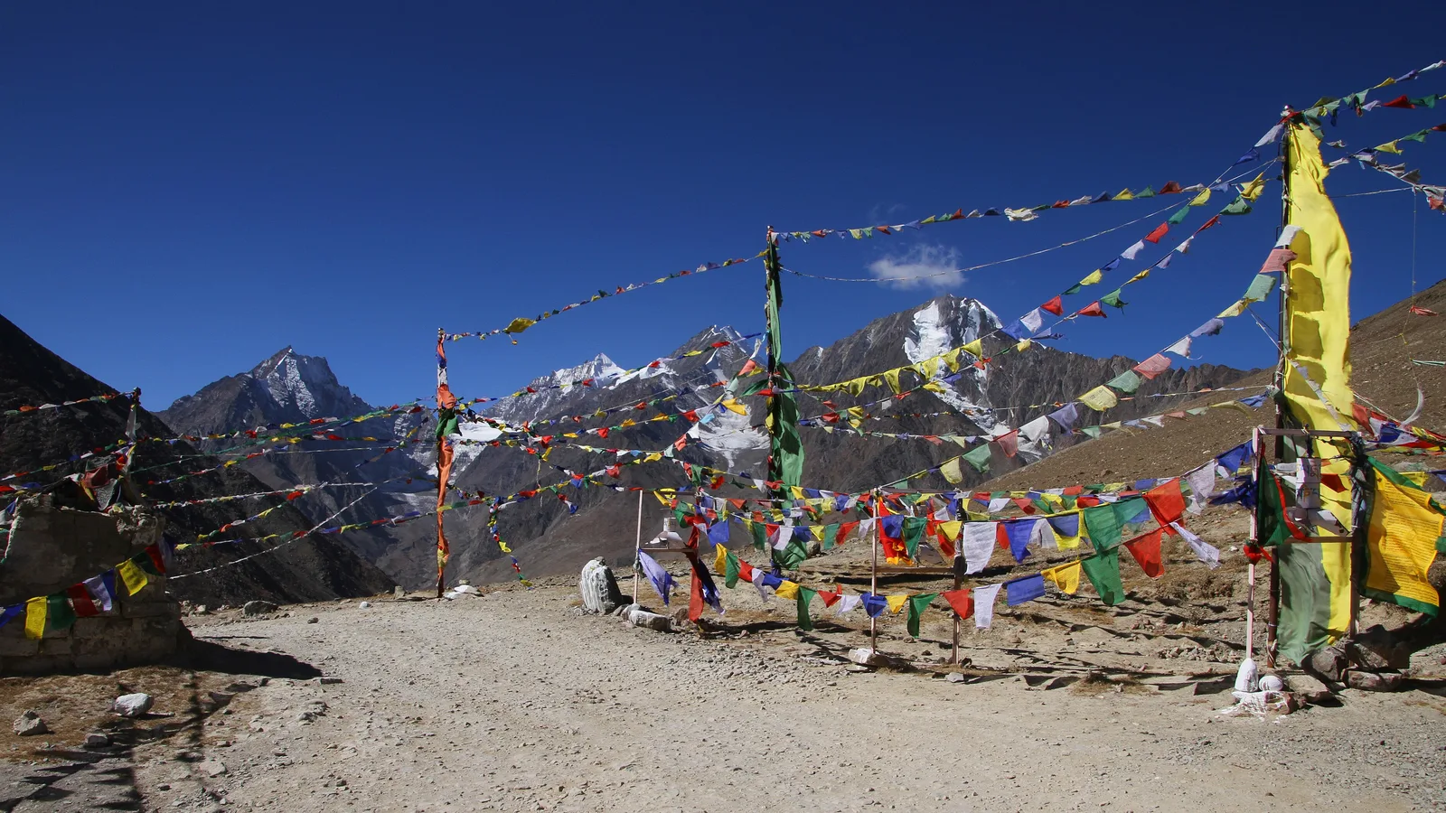 Prayer flags strung between chortens at the top of Kunzum Pass on the Manali to Spiti road, with snow-capped peaks and a clear October sky