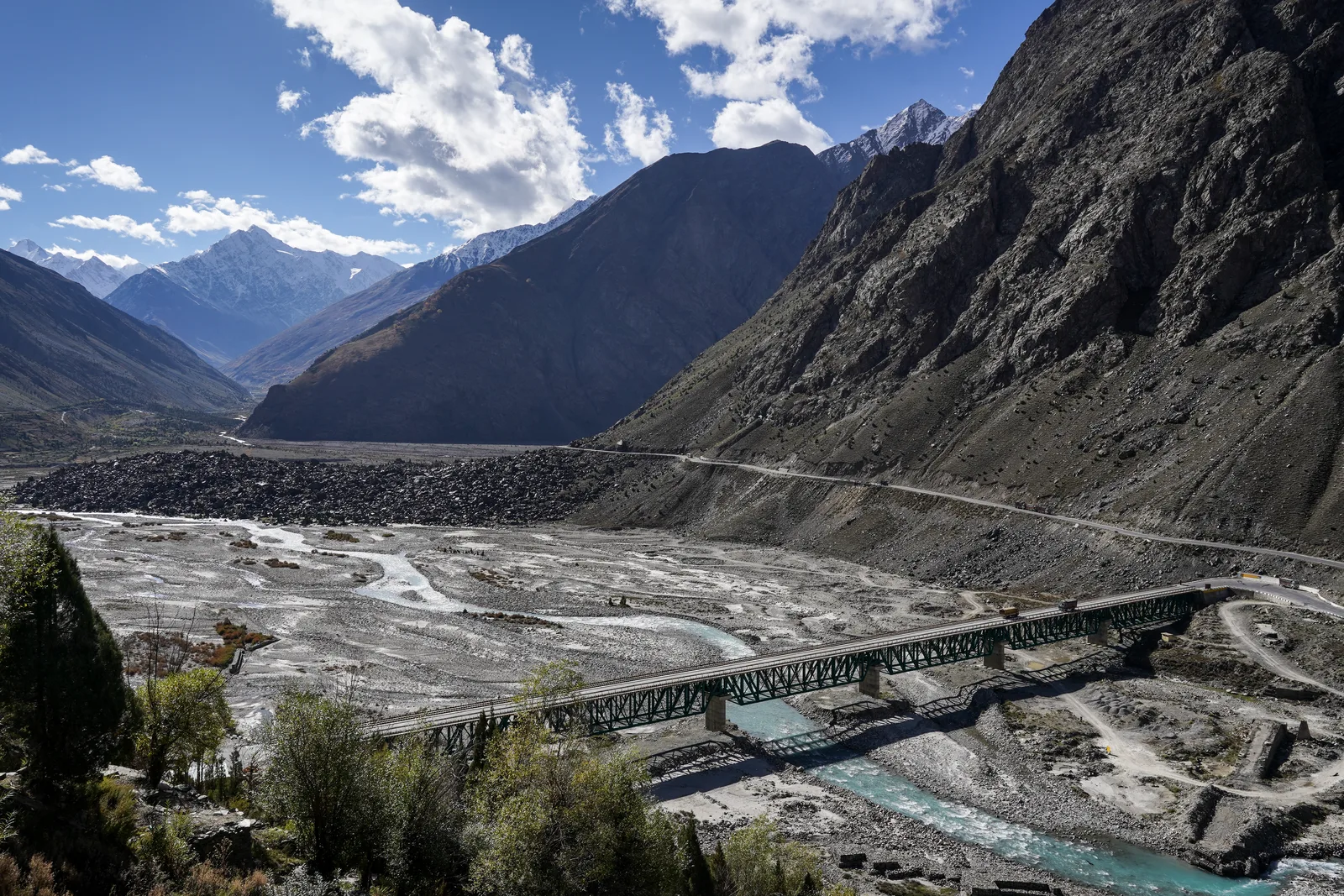 A steel girder bridge over the braided Bhaga river near Darcha in Lahaul with the highway climbing the dark mountainside behind