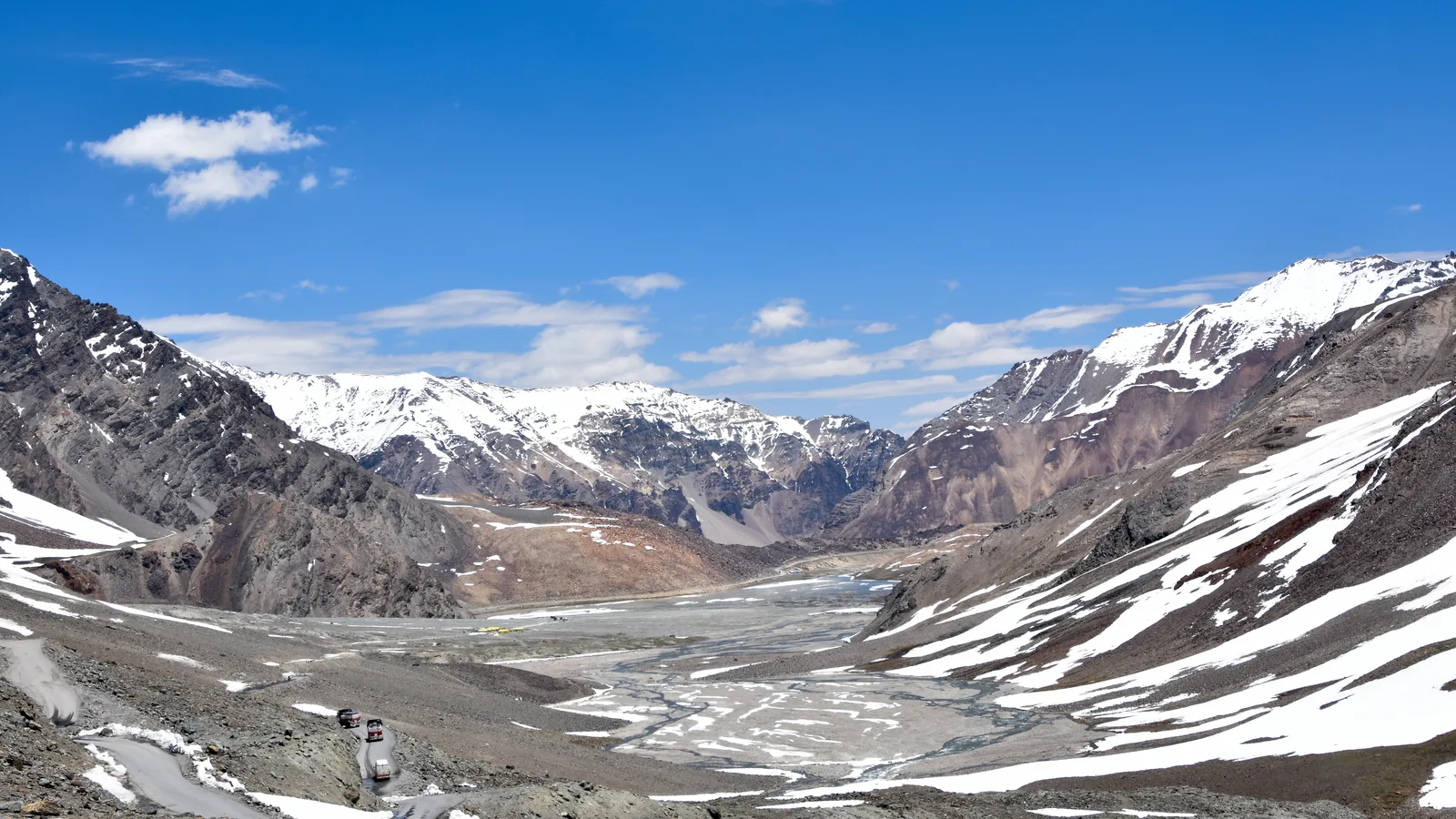 The Manali-Leh highway winding north from Baralacha La between brown slopes streaked with snow under a blue sky
