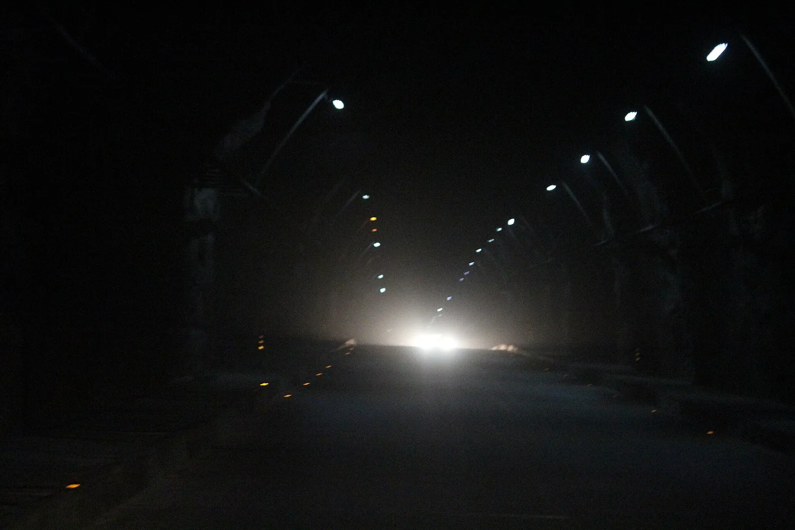 Inside the lit Aut tunnel on the Mandi-Kullu highway with a line of ceiling lights leading to the bright tunnel exit
