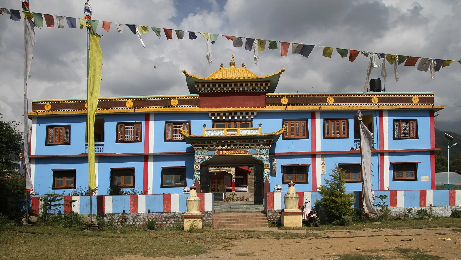 Blue and white Tibetan monastery building with red window frames and prayer flags at Bir in Himachal Pradesh
