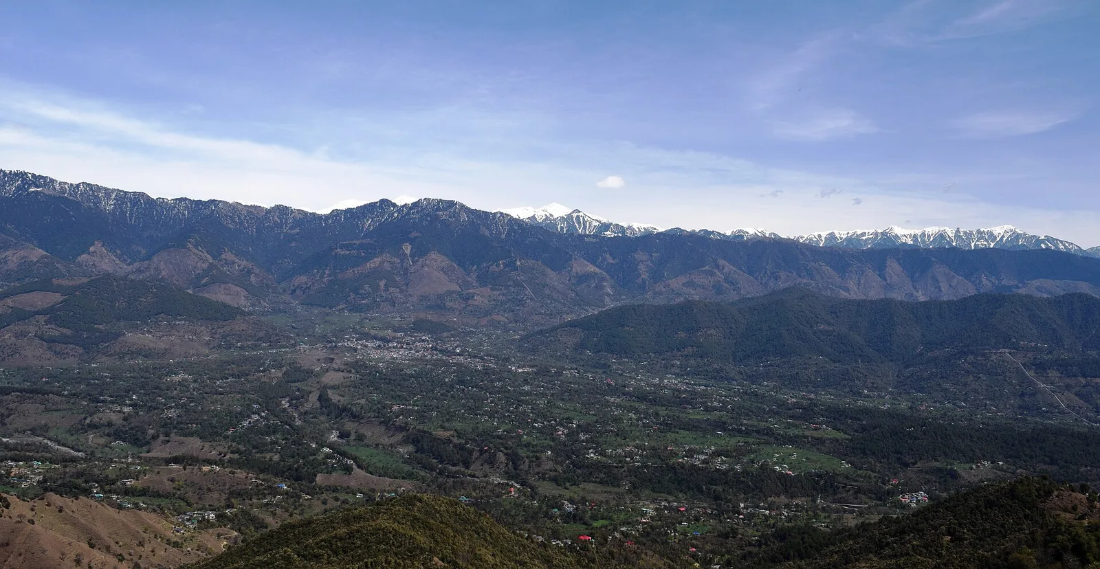 Wide view over Joginder Nagar town and its valley with terraced fields, scattered houses and mountain ridges under a blue sky