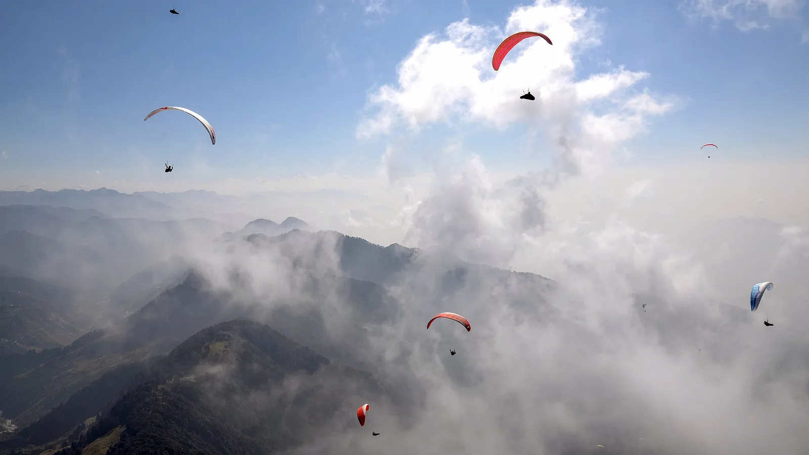 Several paragliders flying above a sea of clouds over forested ridges near Bir in Himachal Pradesh