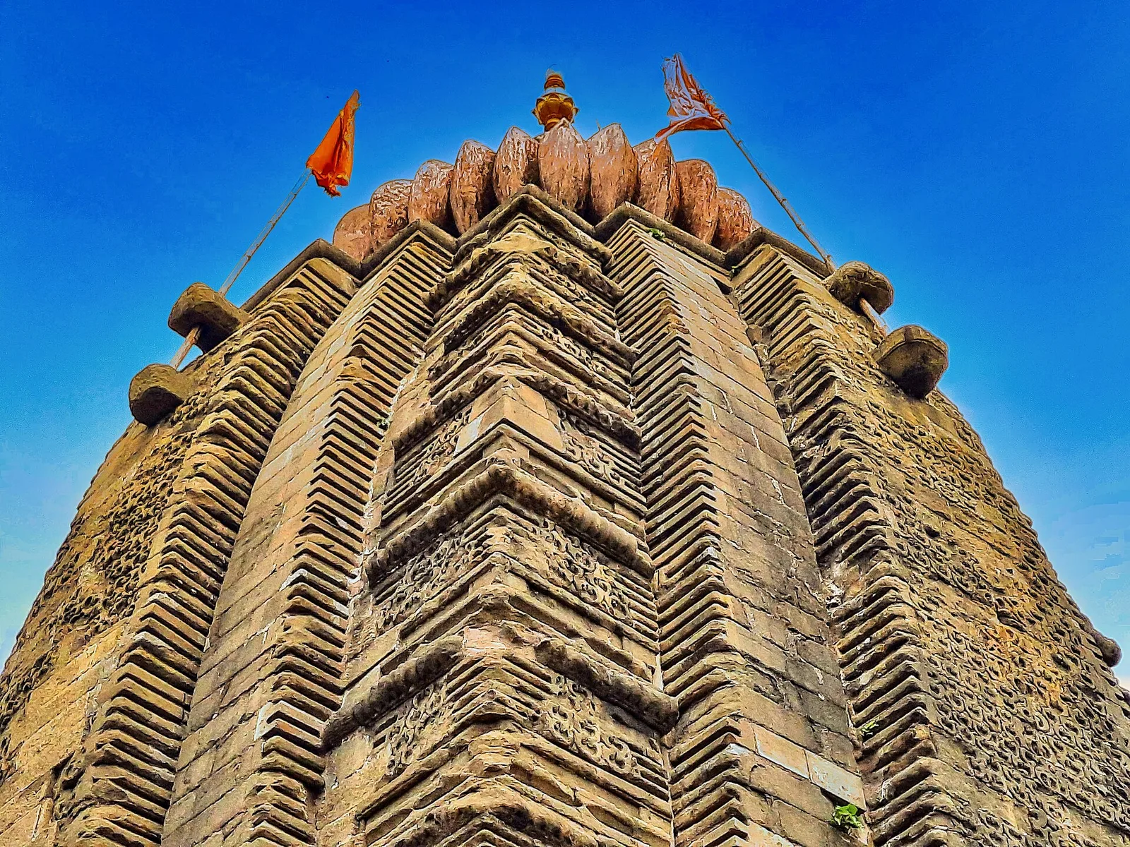 Carved stone spire of the Baijnath temple with saffron flags against a deep blue sky