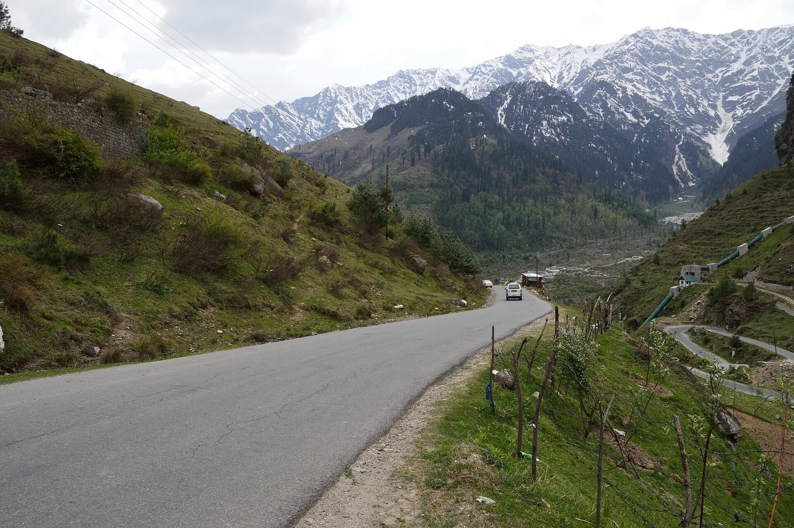 The Leh-Manali highway near Kothi winding through a green valley towards snow-capped mountains, with a single car on the road