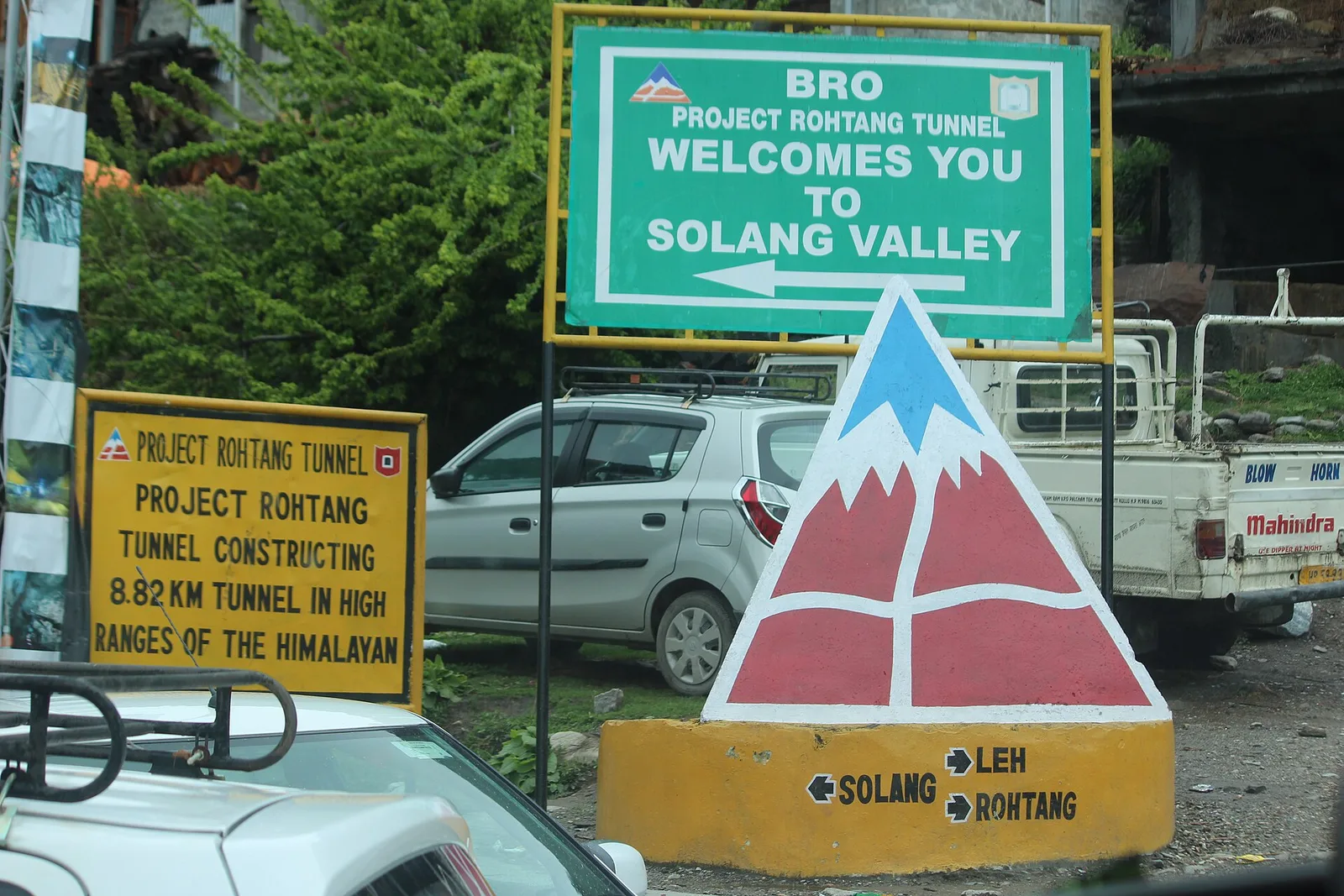 Road signs at the fork near Palchan pointing left to Solang Valley and right to Leh and Rohtang, with a Project Rohtang Tunnel board and parked cars