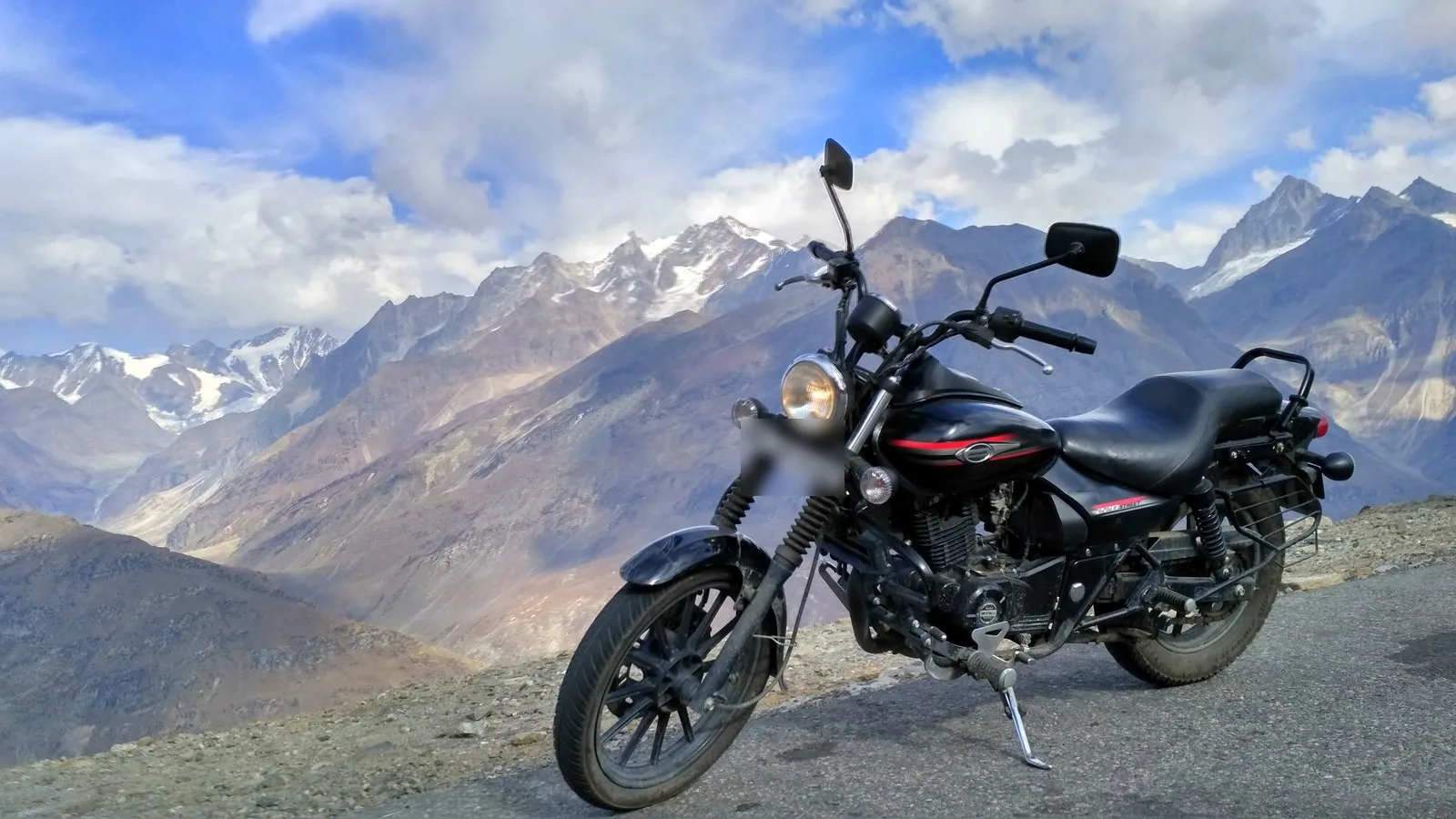 A black cruiser motorcycle parked on the Rohtang Pass road above Manali in early November, with dry brown slopes and snow-capped peaks behind
