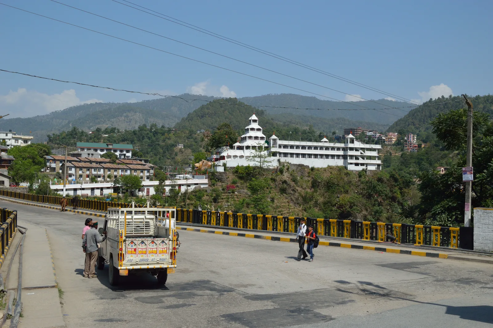 A road bridge over the Beas at Mandi with a white temple complex across the river and hills behind