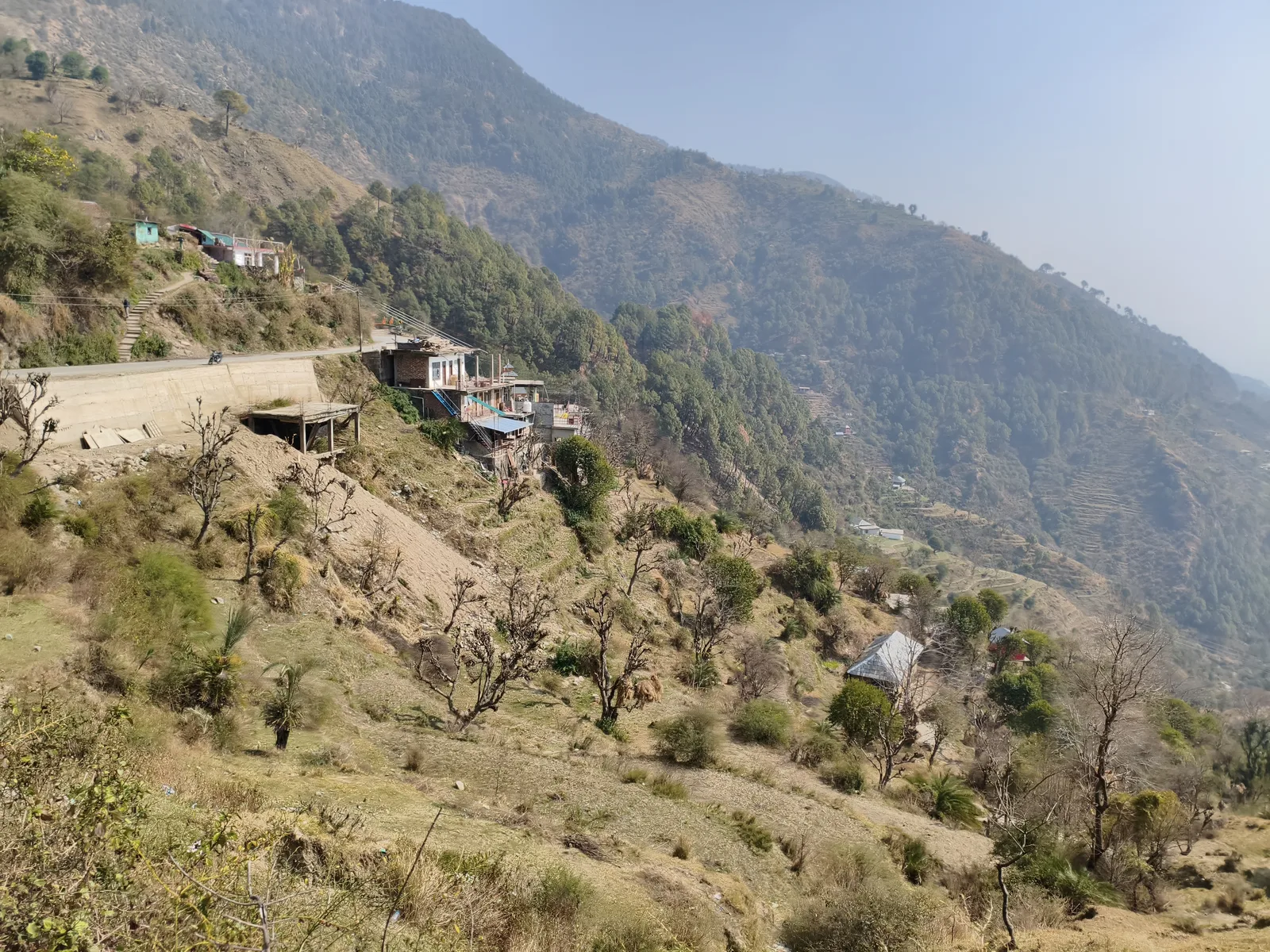 Ghatasani village on a dry hillside with a road cut into the slope and mountains in the distance
